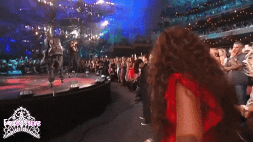 a woman in a red dress is standing on a stage in front of a crowd and the word compulsive is on the bottom right