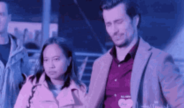 a man in a suit and a woman in a pink jacket are standing next to each other and holding hands .