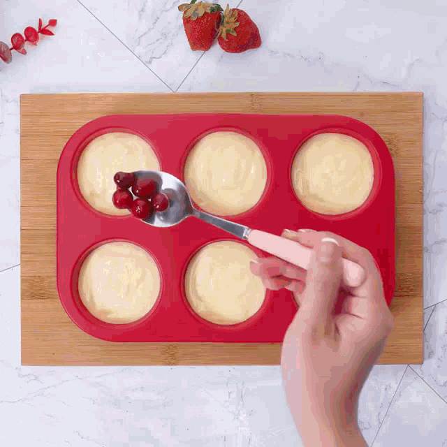 a person is using a spoon to add berries to a muffin pan