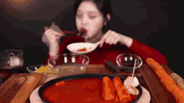 a woman is sitting at a table eating food with chopsticks and a spoon .