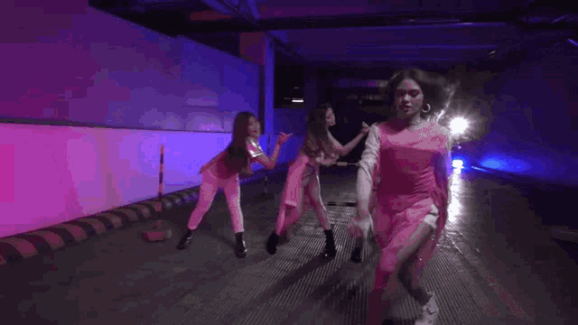 a group of young women are dancing in a dark room with pink lights .
