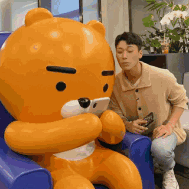 a man is sitting next to a giant teddy bear looking at his phone