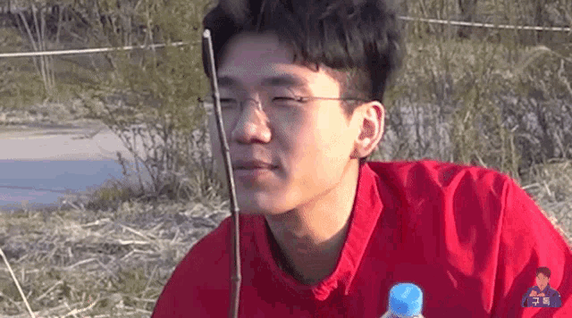 a young man wearing glasses and a red shirt is holding a fishing rod in his hand .