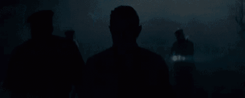 a man in a suit is standing in the dark with a group of police officers behind him .