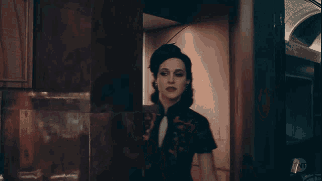 a woman in a black hat and a black dress stands in a dark room