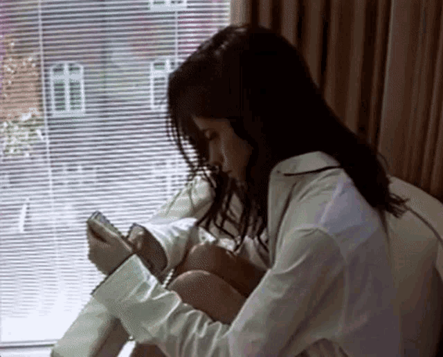 a woman in a white shirt sits in front of a window