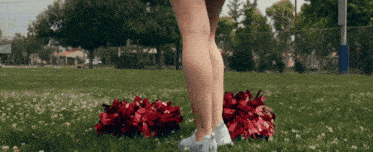 a cheerleader is standing in the grass with pom poms on her feet