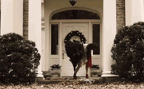 a woman is carrying a christmas tree in front of a white door
