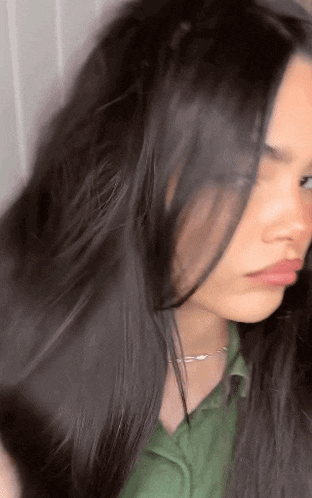 a woman with long black hair is wearing a green shirt and necklace .