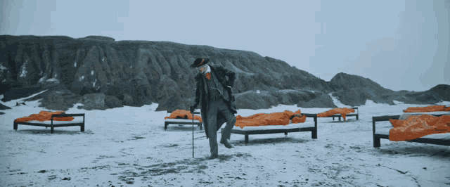 a man in a suit and hat is walking in the snow with a cane