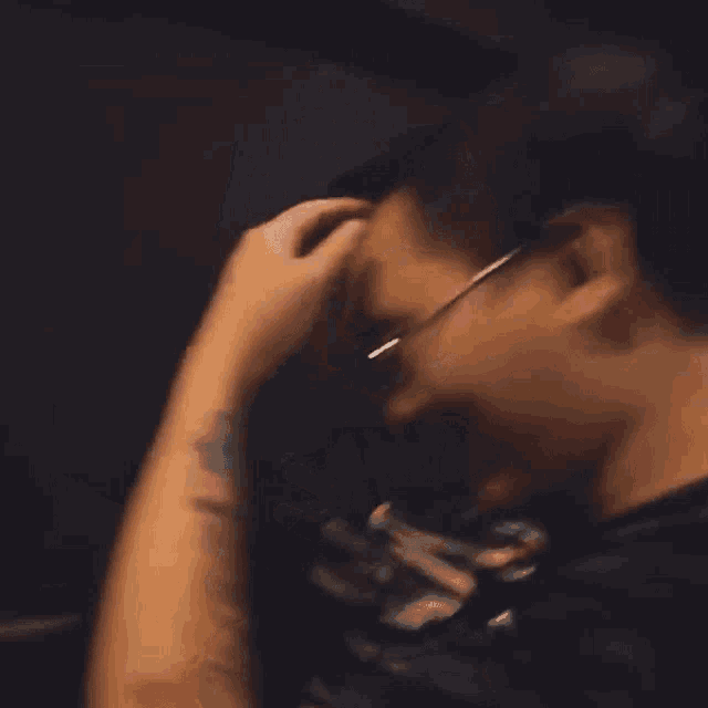 a man wearing glasses is touching his head with his hand .