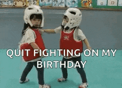 two little girls are fighting each other in a gym and they are wearing helmets .