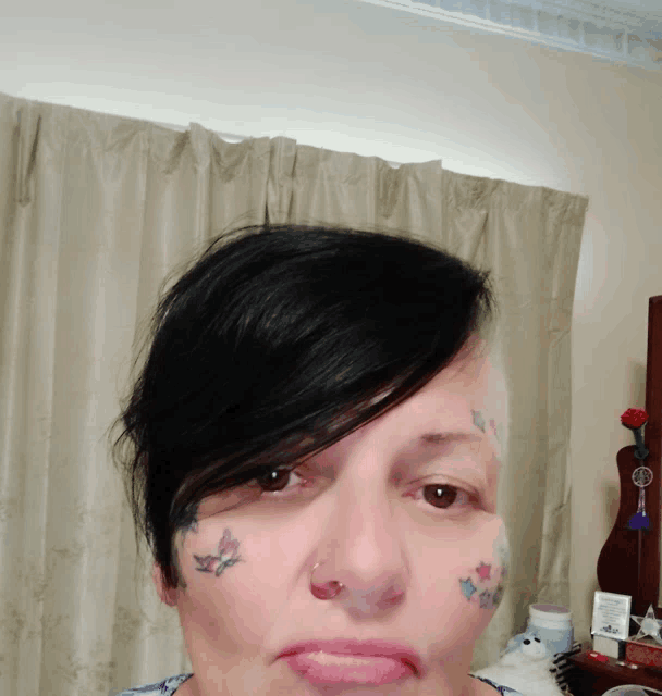 a woman with a butterfly tattoo on her face is looking at the camera