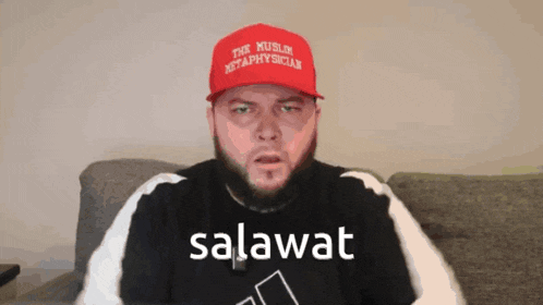 a man wearing a red hat that says the muslim methaphysician is sitting on a couch