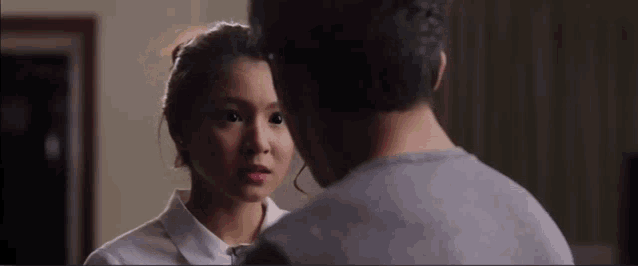 a man and a woman are looking at each other in a room . the woman is wearing a white shirt .