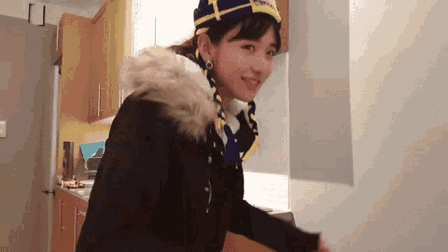 a woman wearing a black jacket and a blue hat with a yellow letter t on it