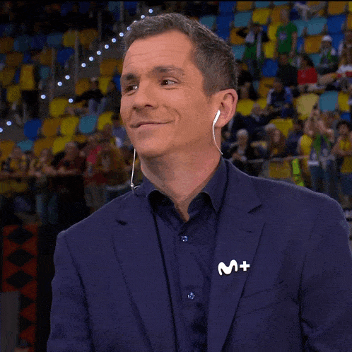 a man wearing ear buds and a blue suit has a m + pin on his jacket