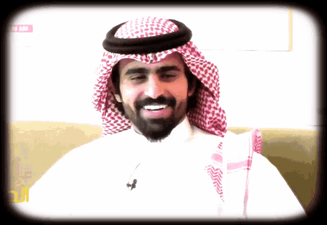 a man with a beard wearing a head scarf and a white shirt smiles