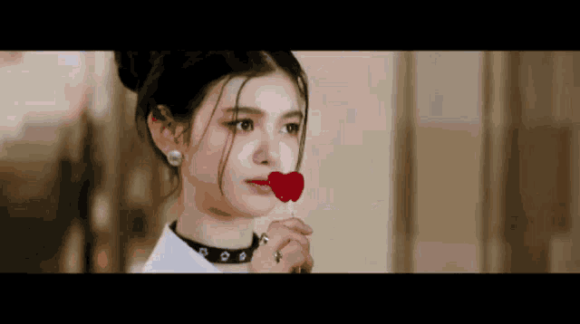 a woman is holding a red heart shaped lollipop in her mouth .