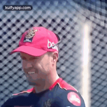 a man wearing a red baseball cap is standing in front of a fence .