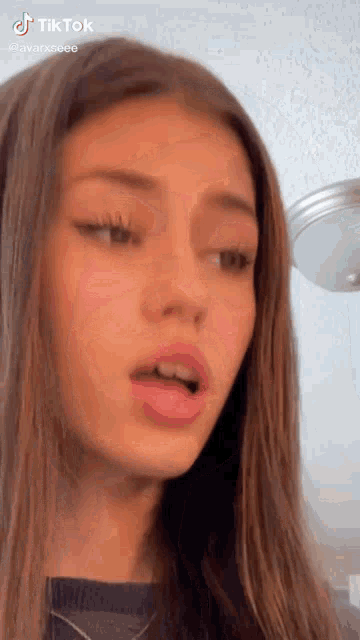 a young girl with long brown hair is making a funny face while looking at the camera .
