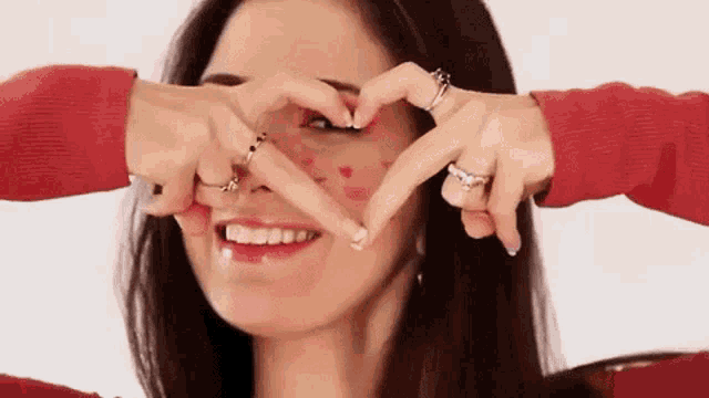 a woman is making a heart shape with her hands on her face