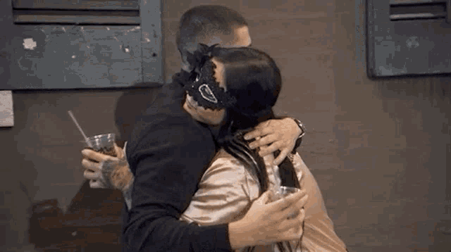 a man and a woman are kissing in front of a building while the woman is wearing a mask .