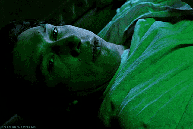 a close up of a person laying in a bed with a green light behind them