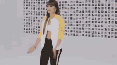 a woman in a yellow and white jacket is dancing in front of a wall with a lot of pictures on it .