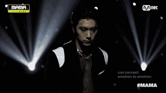 a man in a black suit stands in front of a mnet sign