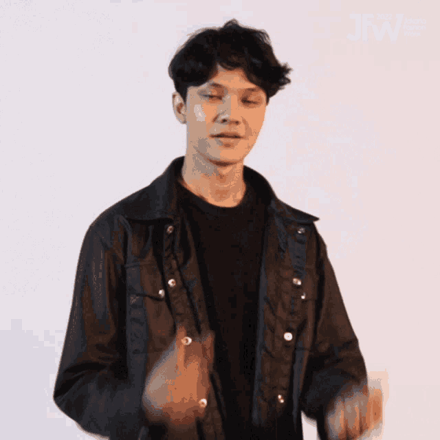 a young man wearing a black jacket and a black shirt is clapping