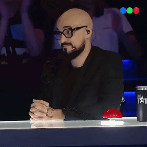 a man with glasses and a beard sits at a table with a cup that says got a talent