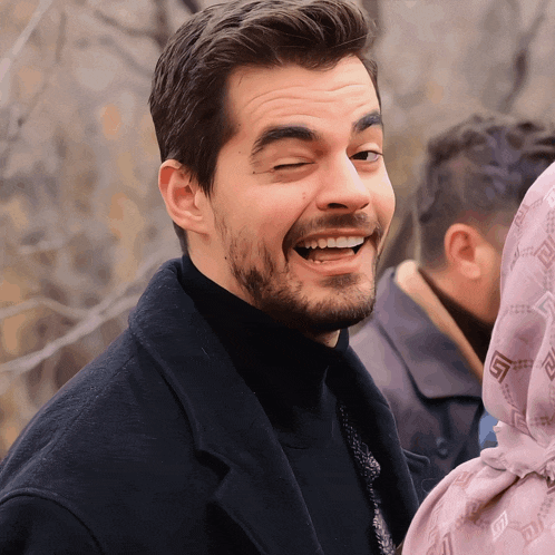 a man with a beard wearing a black turtleneck sweater is smiling