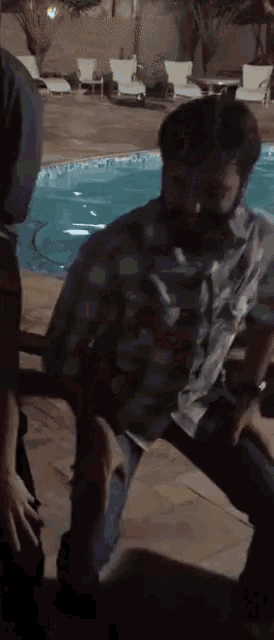 a man with a beard is sitting in front of a swimming pool
