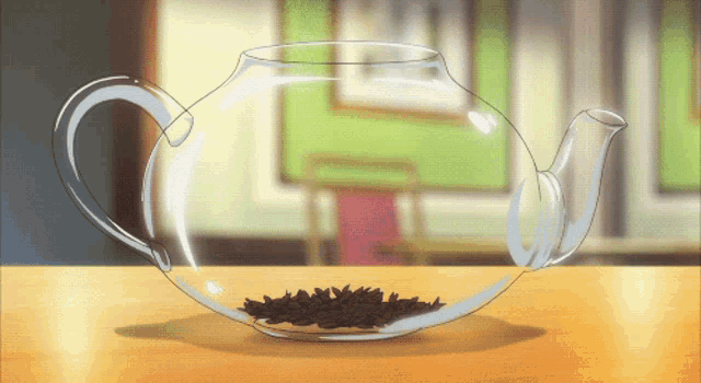 a glass teapot filled with tea leaves sits on a wooden table