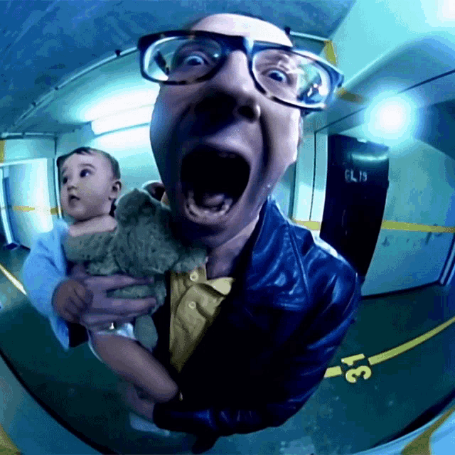 a man with glasses is holding a baby in front of a door with the number 6l19