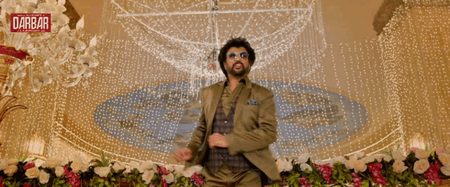 a man in a suit is dancing in front of a chandelier with the word " darbar " on the bottom right