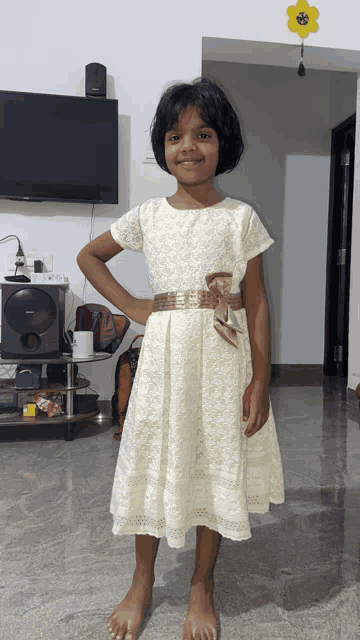 a little girl in a white dress stands in front of a sony television