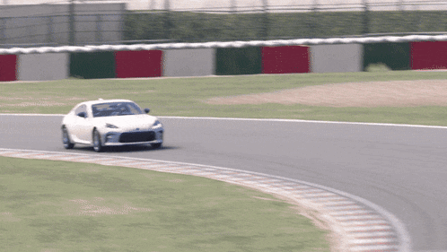 a white car is driving on a track with red green and white barriers