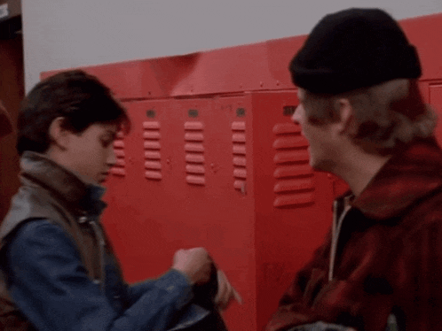 two boys are standing in front of red lockers talking