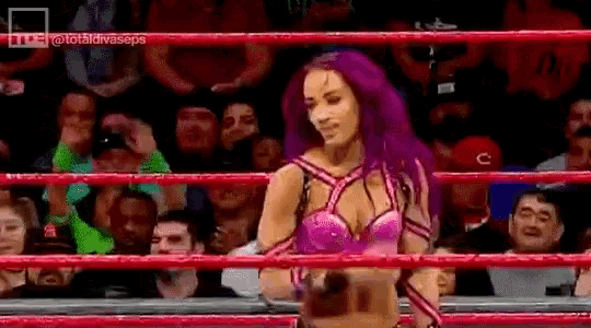 a woman with purple hair is standing in a boxing ring with a crowd behind her .