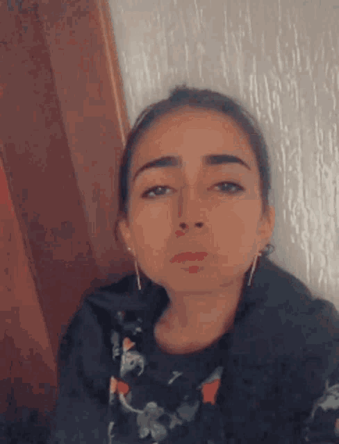 a woman wearing earrings and a black shirt is making a funny face
