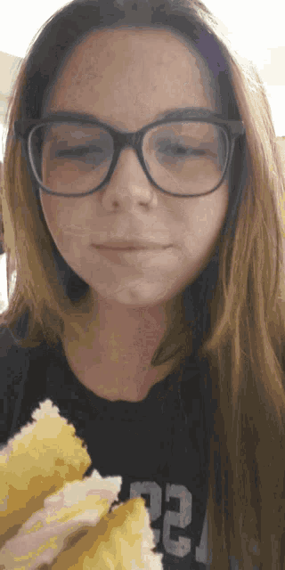 a woman wearing glasses and a black shirt with the number 22 on it is eating a sandwich