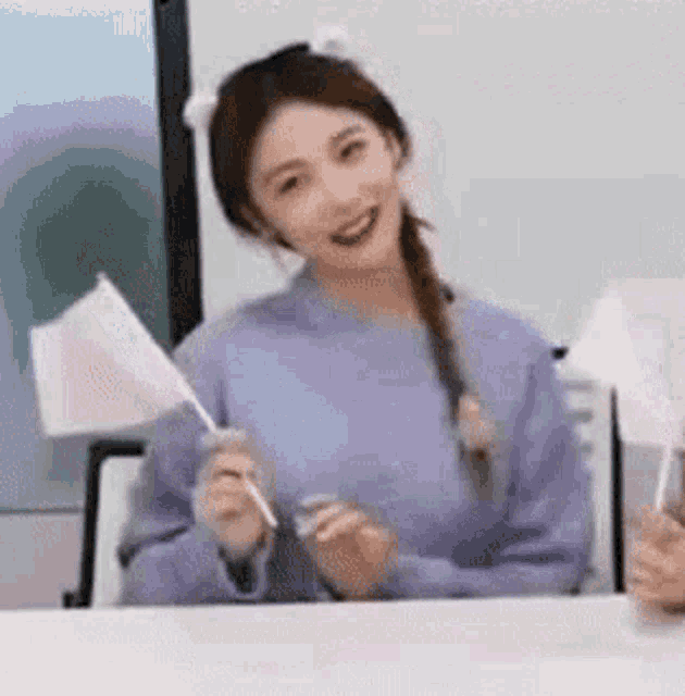 a woman in a purple sweater is sitting at a table holding a small white flag .