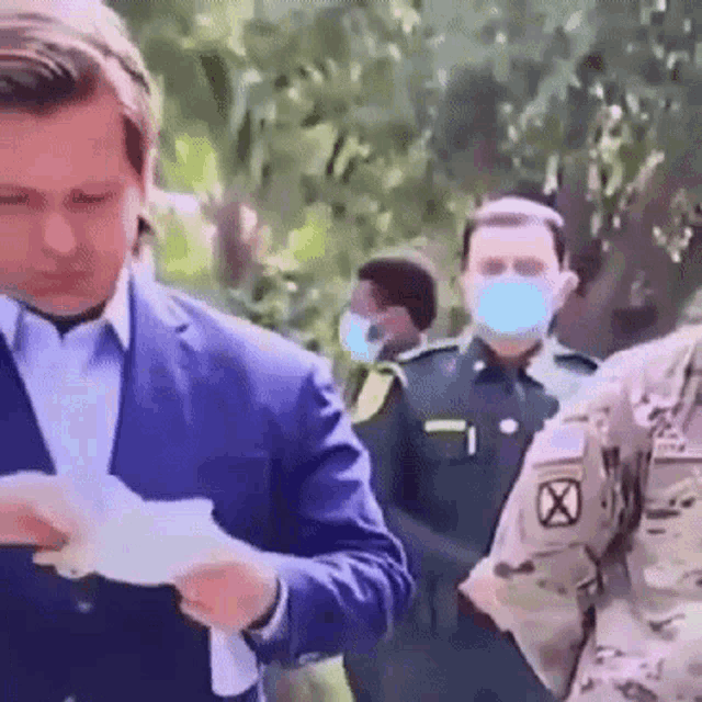a man in a suit is holding a piece of paper in front of a group of men wearing masks .