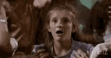 a young girl is making a surprised face while sitting in a crowd .