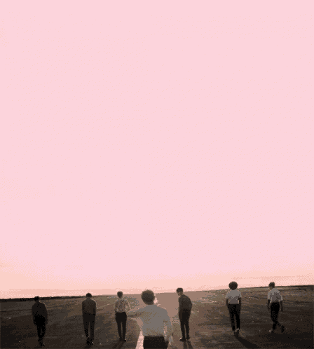 a group of men are walking on a road with a pink background