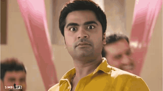 a man in a yellow shirt is making a funny face with the words simbugifs visible in the corner