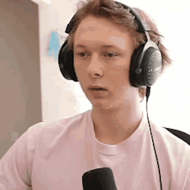 a young man wearing headphones and a pink t-shirt is talking into a microphone .