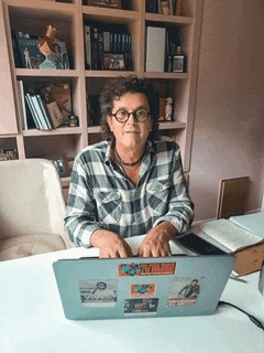 a woman sits at a desk with a laptop with stickers on it